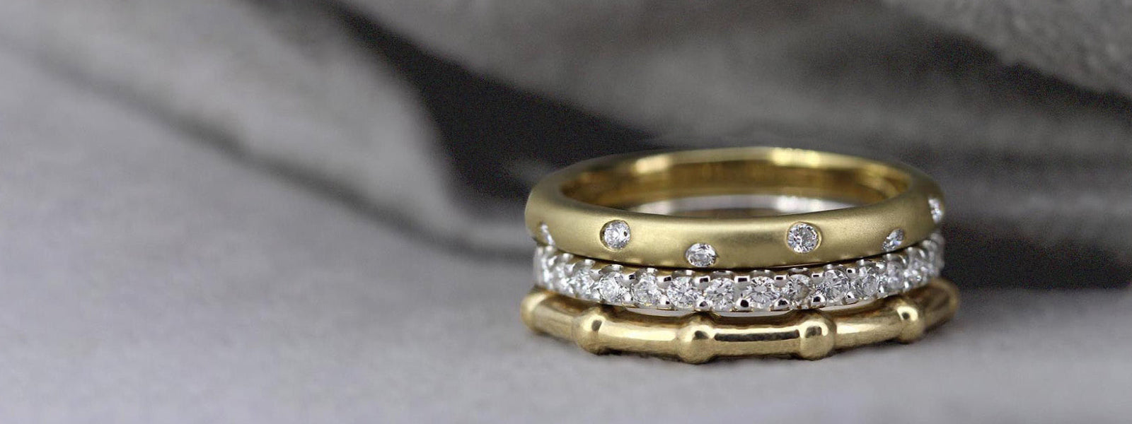 Stack of gold and silver rings with diamonds on a textured gray background